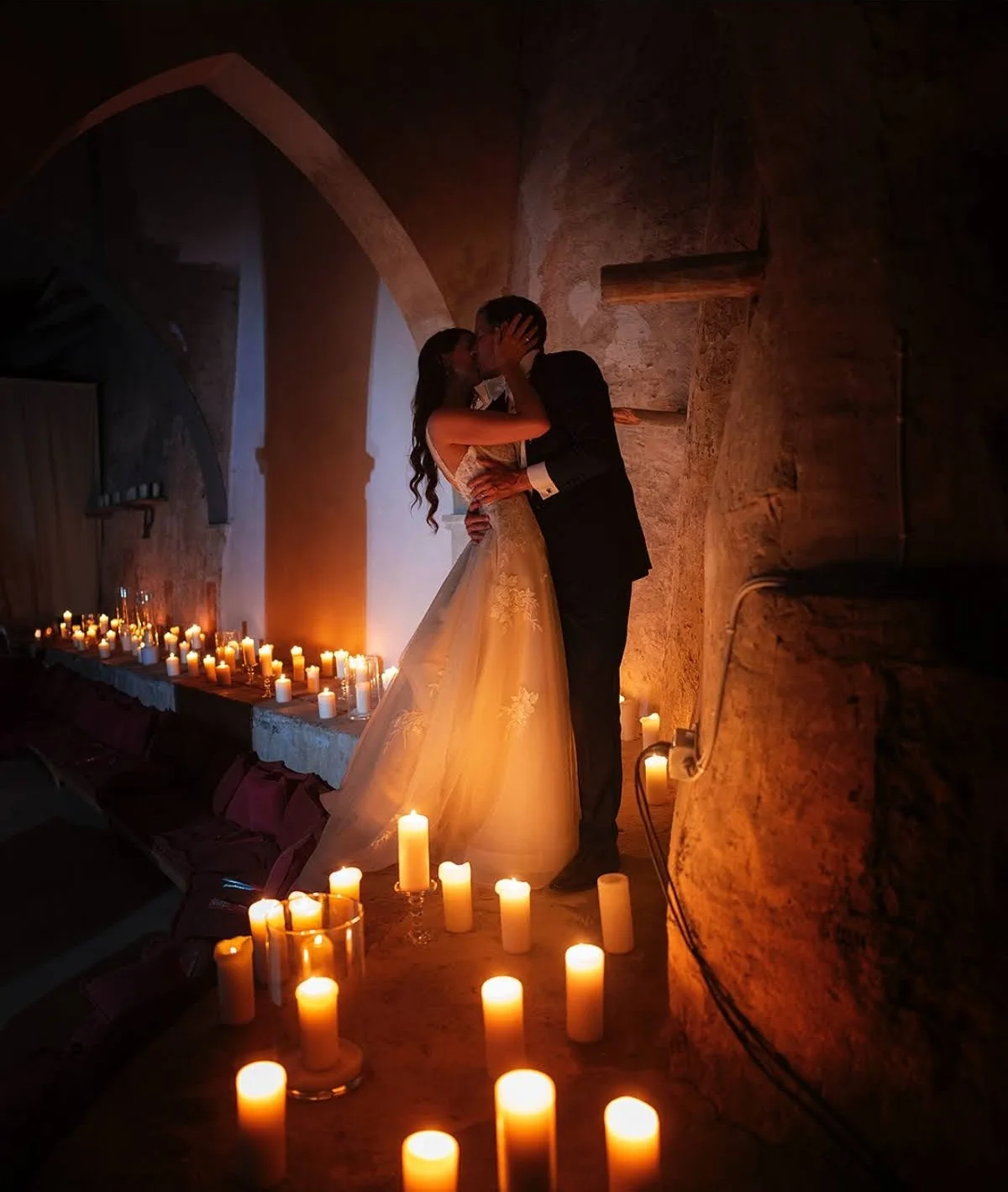 Bride and groom kissing surrounded by candles under a stone arch