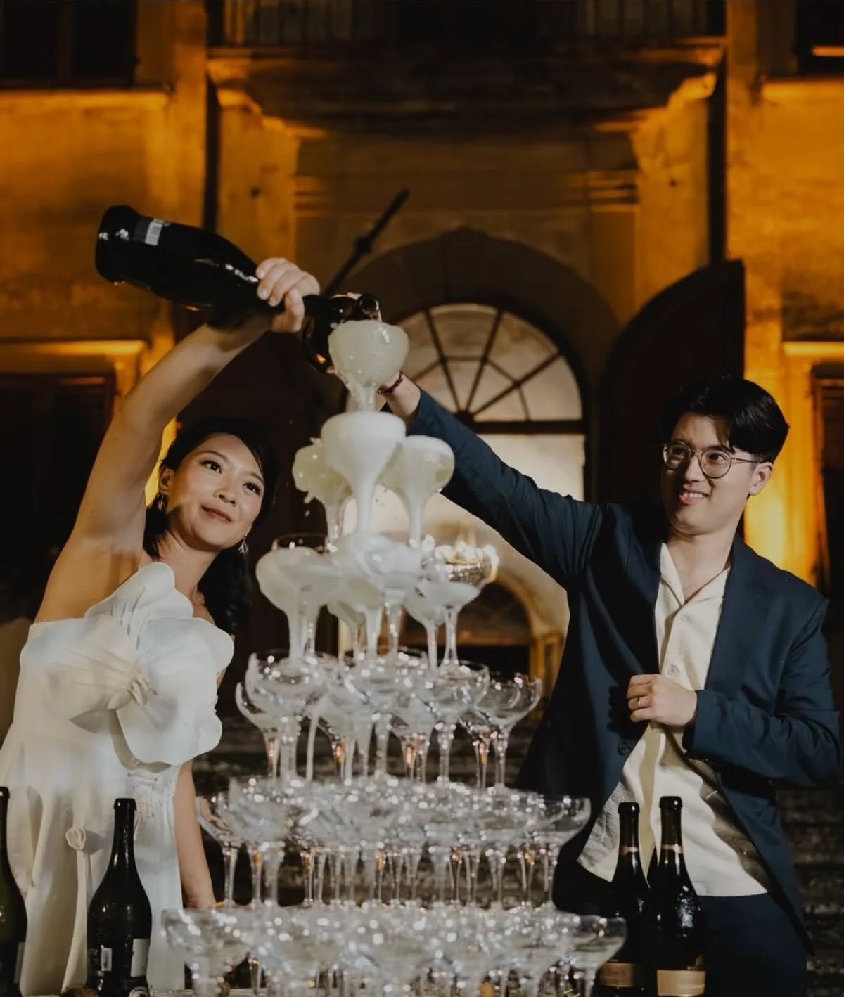 Sposi che versano una torre di champagne davanti a una villa, di sera