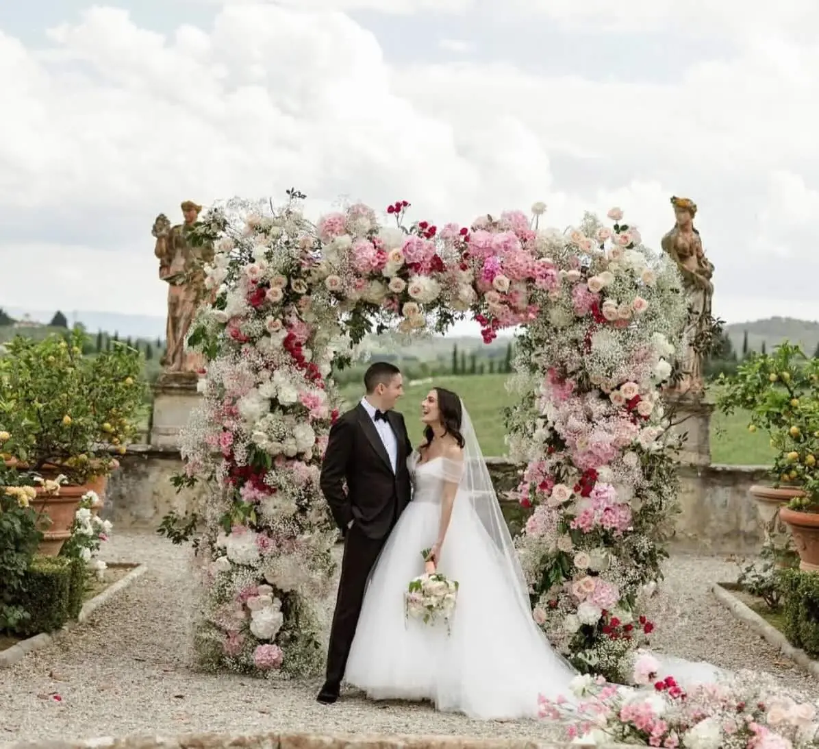 Sposi sotto un arco di fiori rosa sulla terrazza di una villa toscana con statue