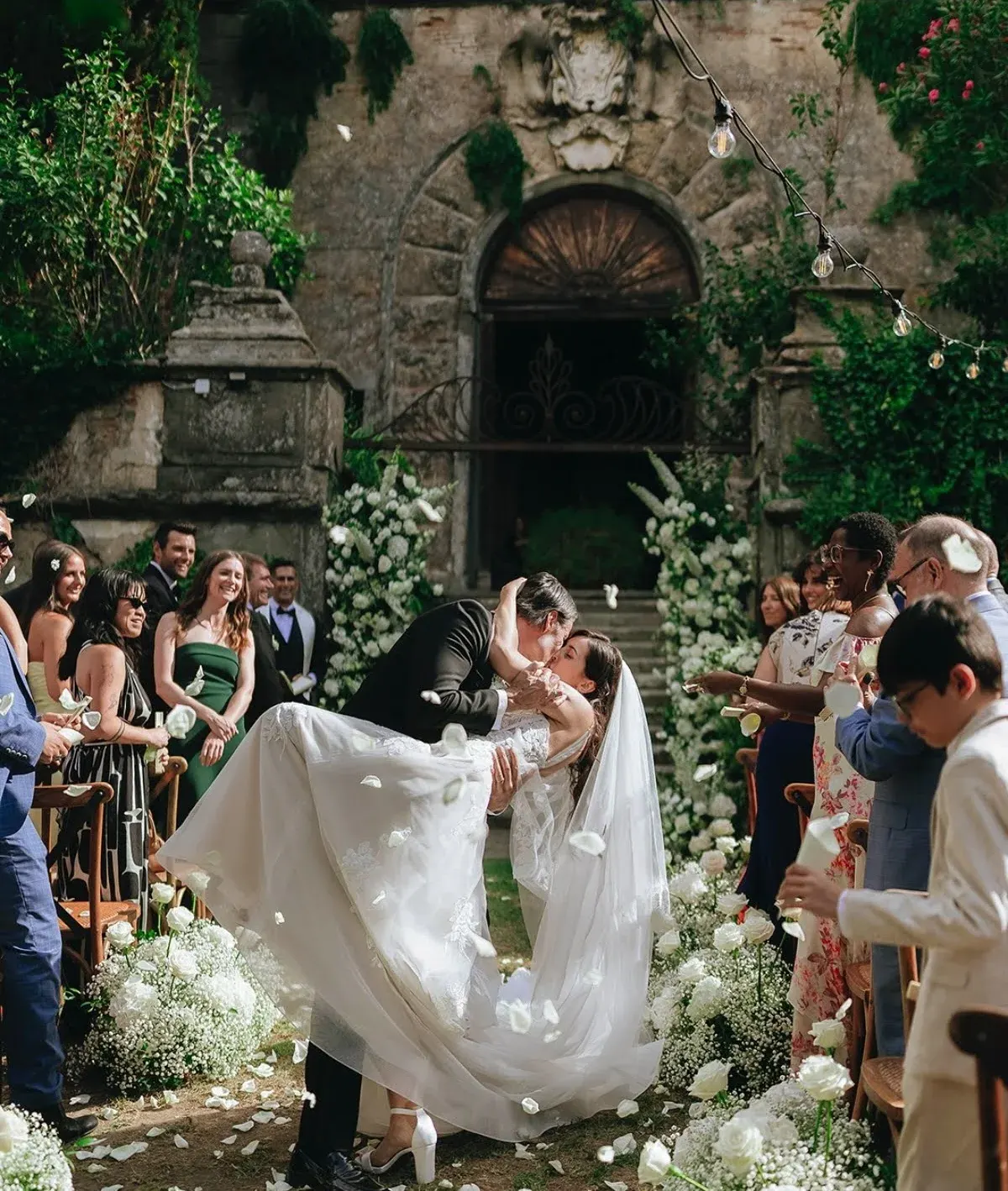 Efffetti® | Wedding Planner in Italy & Tuscany Bride and groom kissing as guests throw petals after the ceremony at a historic villa