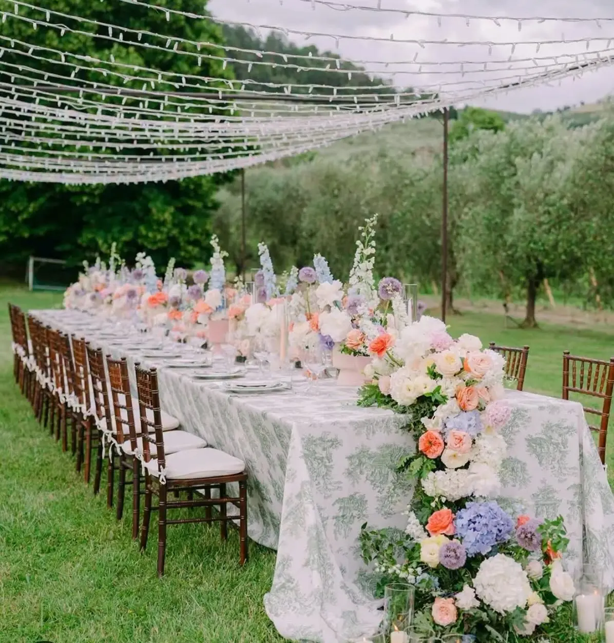 Long wedding table with pastel flowers under string lights in an olive grove